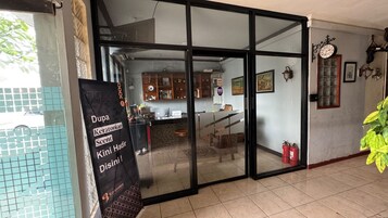 A room with a sliding glass door leading to a kitchen area, a black sign with text, a clock on the wall, and a potted plant.