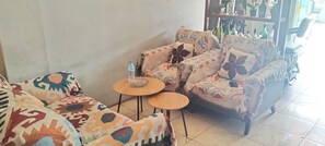 Un salón con sofás estampados, dos mesas redondas de madera y una estantería con objetos decorativos.