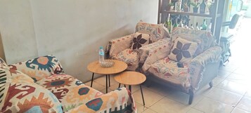 Un salón con sofás estampados, dos mesas redondas de madera y una estantería con objetos decorativos.