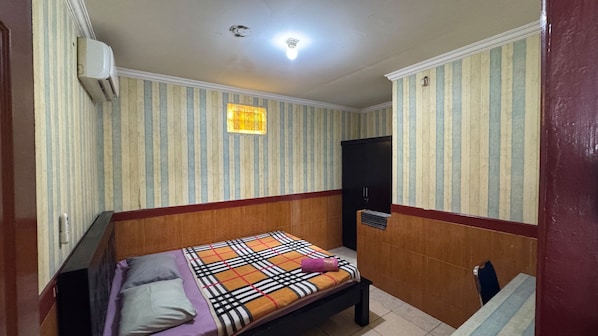 Una habitación pequeña con cama individual, papel tapiz a rayas, cabecera de madera, mesita de noche y una lámpara en el techo.