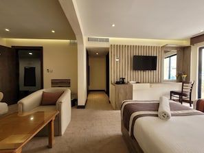 A hotel room with a bed, a sofa, a desk, a television, and a window with a view. - Petra Edom Hotel (Wadi Musa)