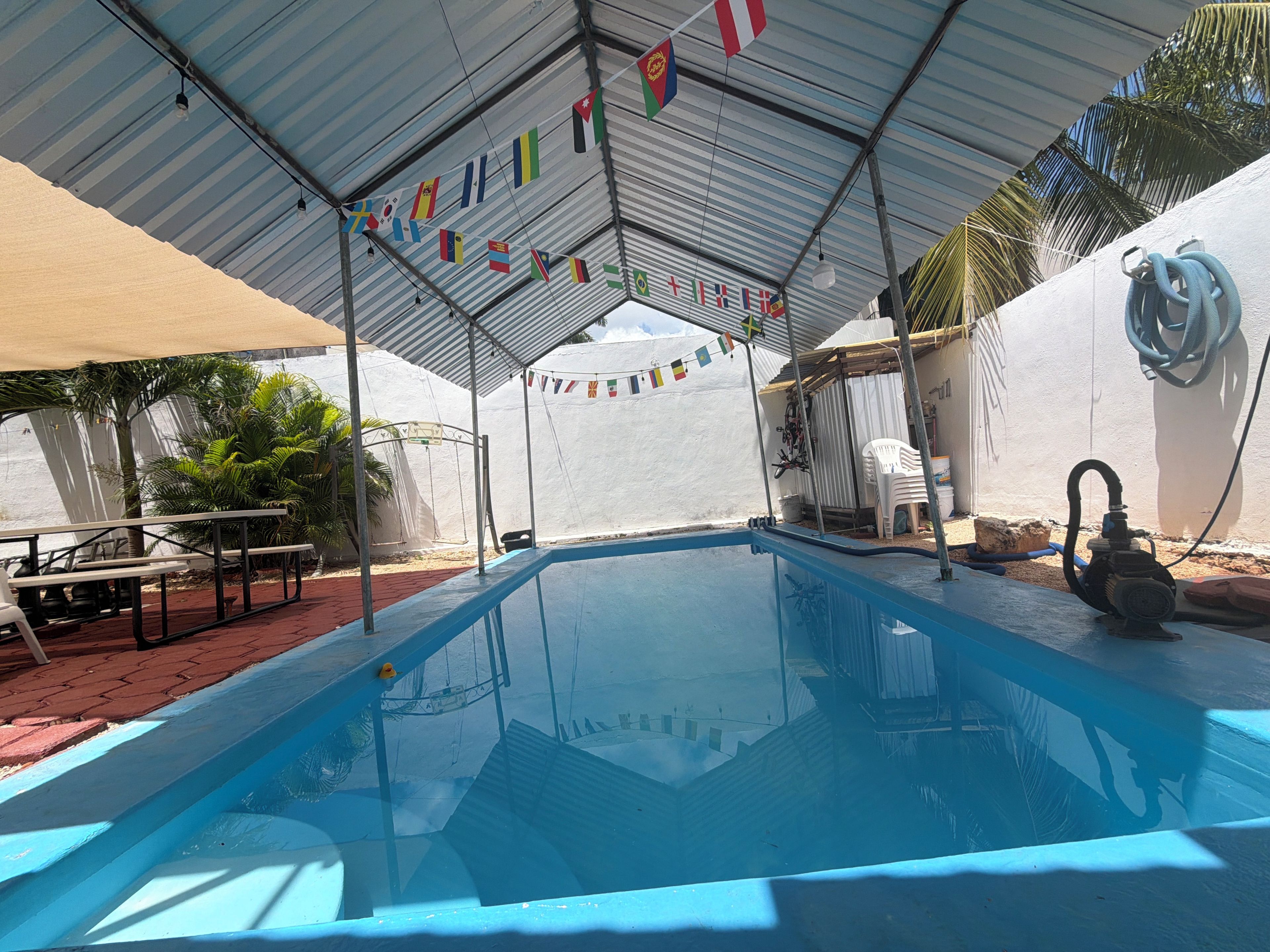 A swimming pool with a covered area, flags, and a hose.