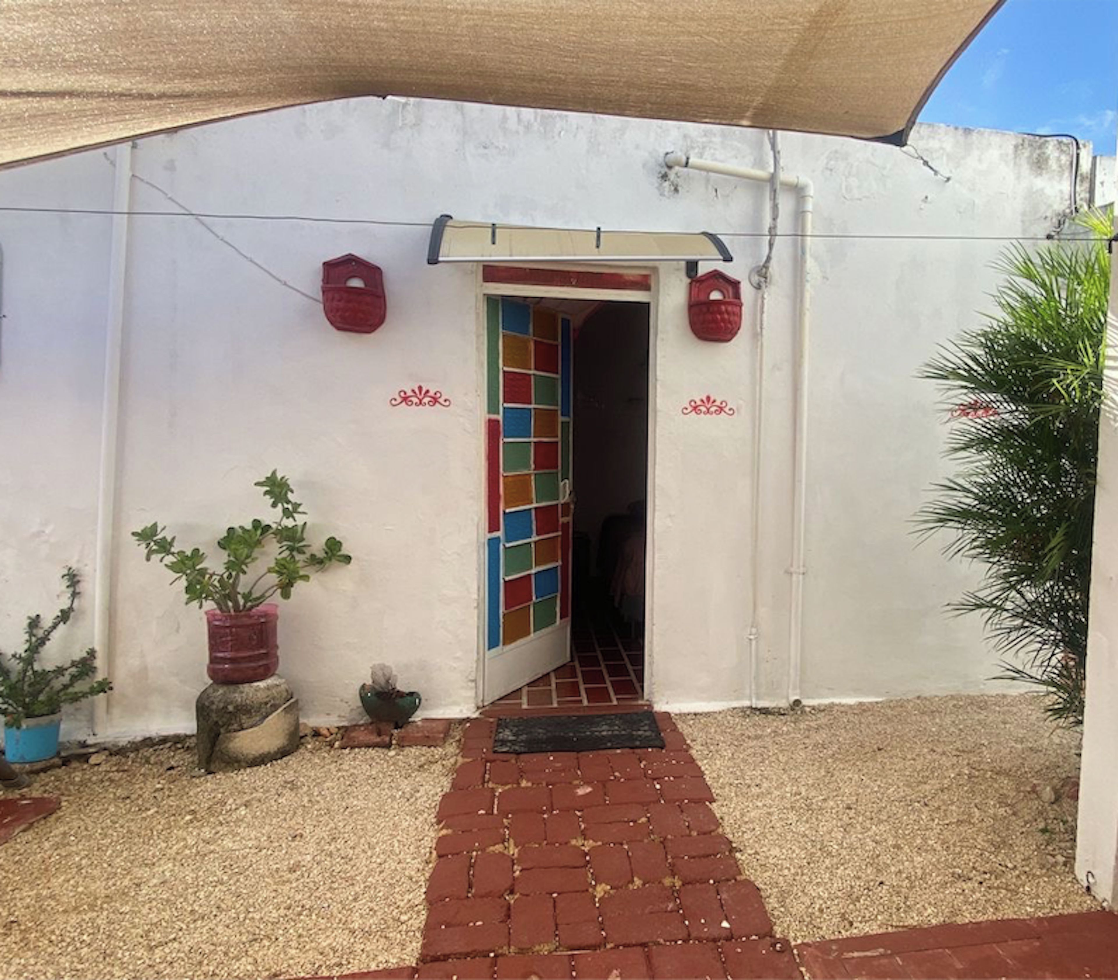 A building entrance with a tiled door, a red brick pathway, and potted plants.