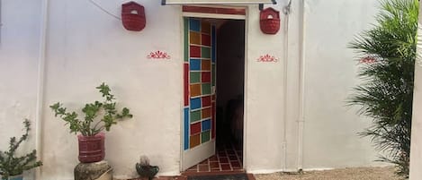A building entrance with a tiled door, a red brick pathway, and potted plants.