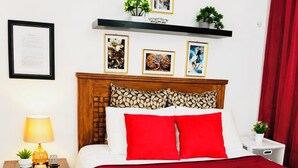 Une chambre d’hôtel avec un lit, une table de chevet, une lampe, une couverture rouge et un rideau rouge.