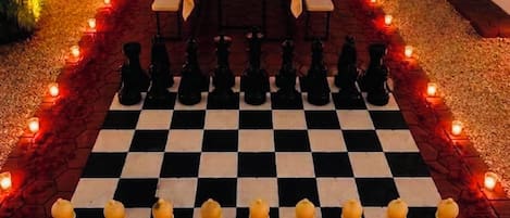 A checkered chessboard with pieces arranged for a game, surrounded by candles and a table with a floral centerpiece.