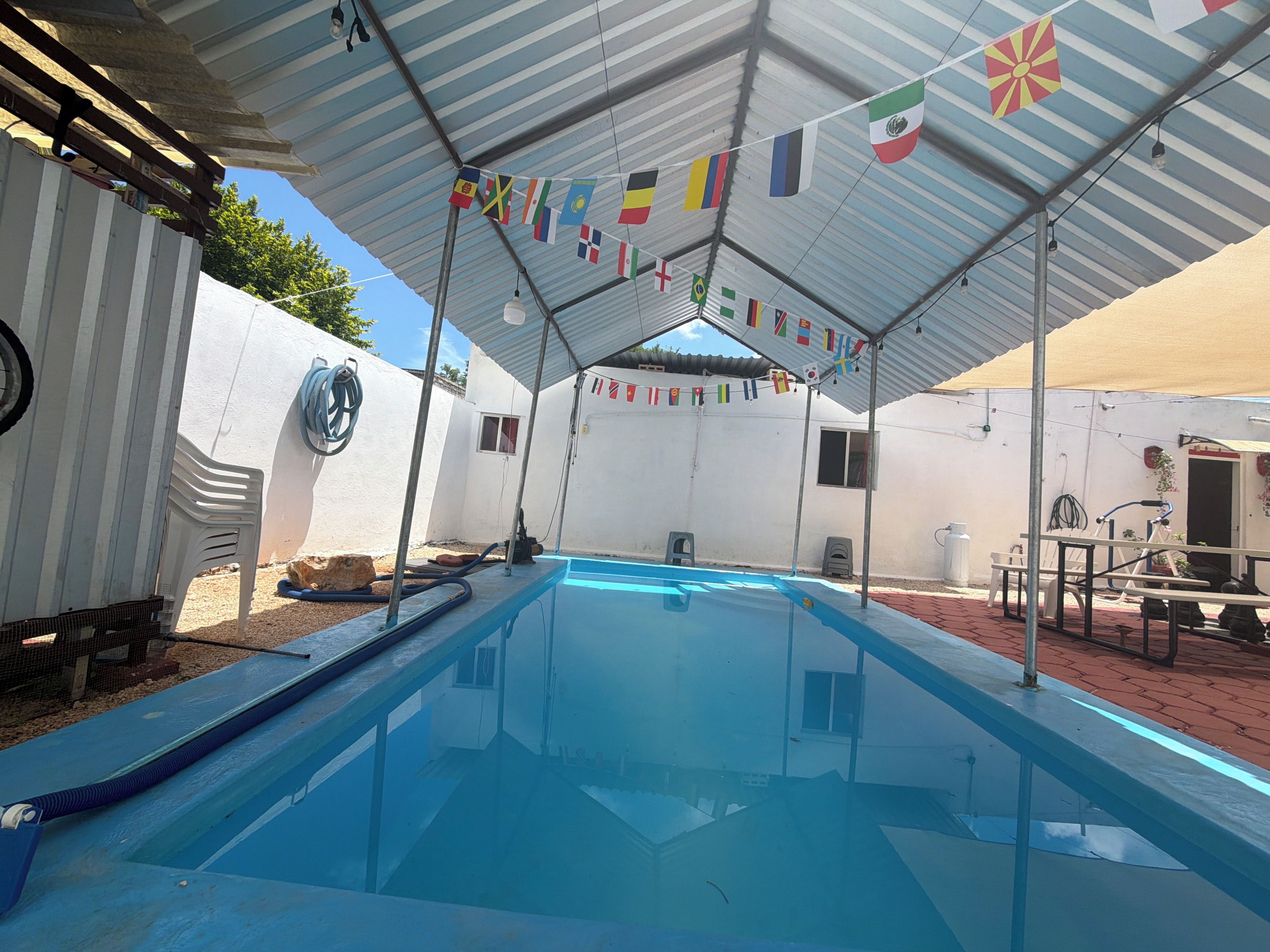 A swimming pool under a covered area with flags, surrounded by white walls and a red brick floor.