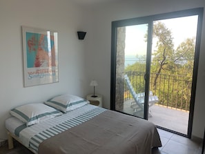 Ein Schlafzimmer mit einem Bett, einem Poster, einem Nachttisch, einer Lampe und einem Balkon mit Blick.