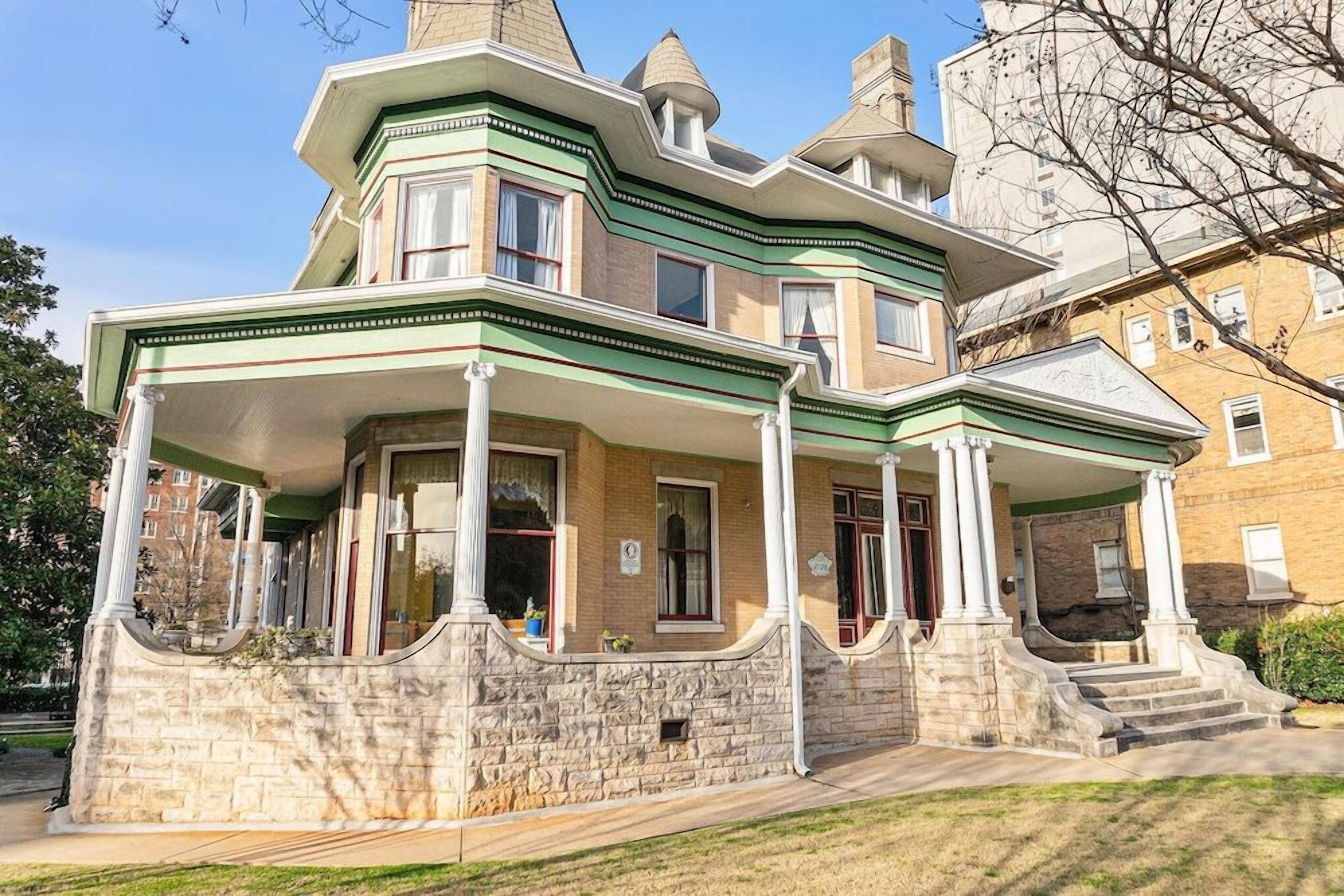 A two-story building with a stone facade, a wrap-around porch, and a symmetrical design.