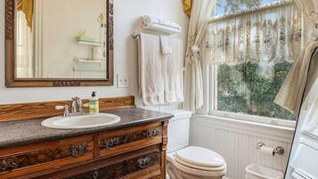 A bathroom with a wooden vanity, a white sink, a mirror, a toilet, and a window with curtains.