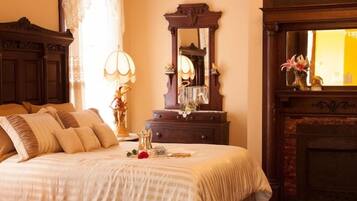 A traditional bedroom with a large bed, a wooden dresser, a mirror, and a fireplace.