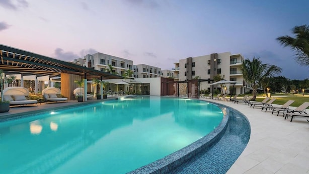 Una piscina con sillones de descanso y un área de estar cubierta, rodeada de edificios modernos.