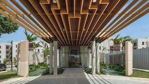 Un pasillo cubierto con techo de madera moderna y paneles de vidrio, que conduce a la entrada de un edificio.