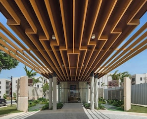 Une allée couverte, dotée d’un plafond en bois moderne et de panneaux de verre, qui mène à l’entrée d’un bâtiment.