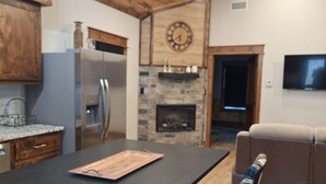 A kitchen with a central island, a stone fireplace, and a television mounted on the wall. - Secluded Sunset a charming rustic 1-bedroom cabin in Ringold (Ringold)