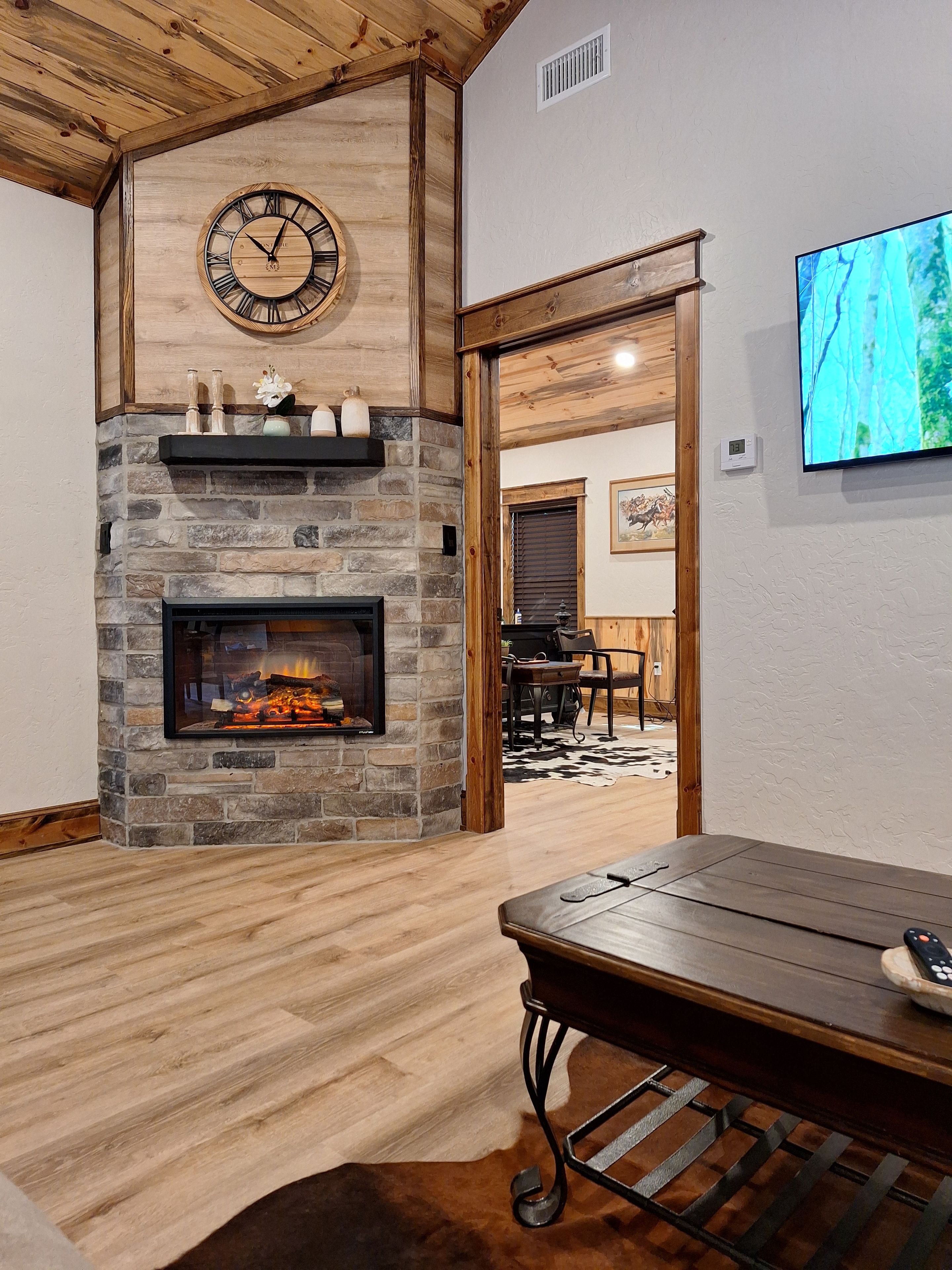 A room with a stone fireplace, a clock, and a television on the wall.
