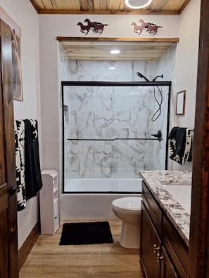 Un bany amb plat de dutxa tancat per vidre, un vàter i un lavabo amb taulell de marbre.