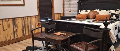 A bedroom with a wooden ceiling, a bed with patterned bedding, a cowhide rug, and a dining table with chairs.