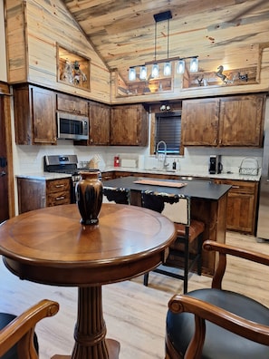 A kitchen with wooden cabinets, a microwave, a coffee maker, and a dining table with chairs. - Secluded Sunset a charming rustic 1-bedroom cabin in Ringold (Ringold)