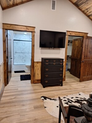 A room with a wooden ceiling, a television mounted on the wall, a wooden cabinet, and a cowhide rug on the floor. - Secluded Sunset a charming rustic 1-bedroom cabin in Ringold (Ringold)