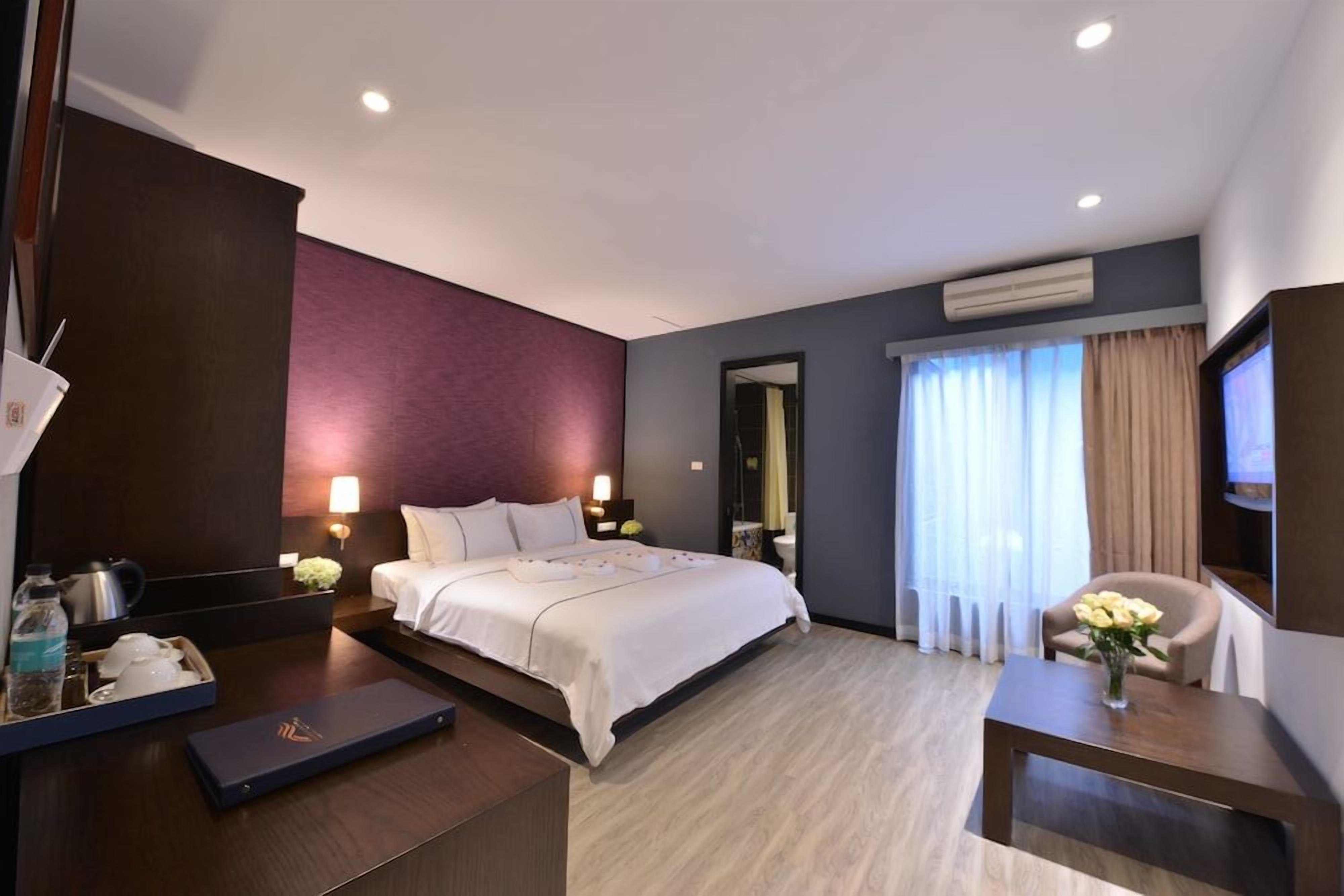 A hotel room with a bed, bedside table, TV, and a desk with a chair.