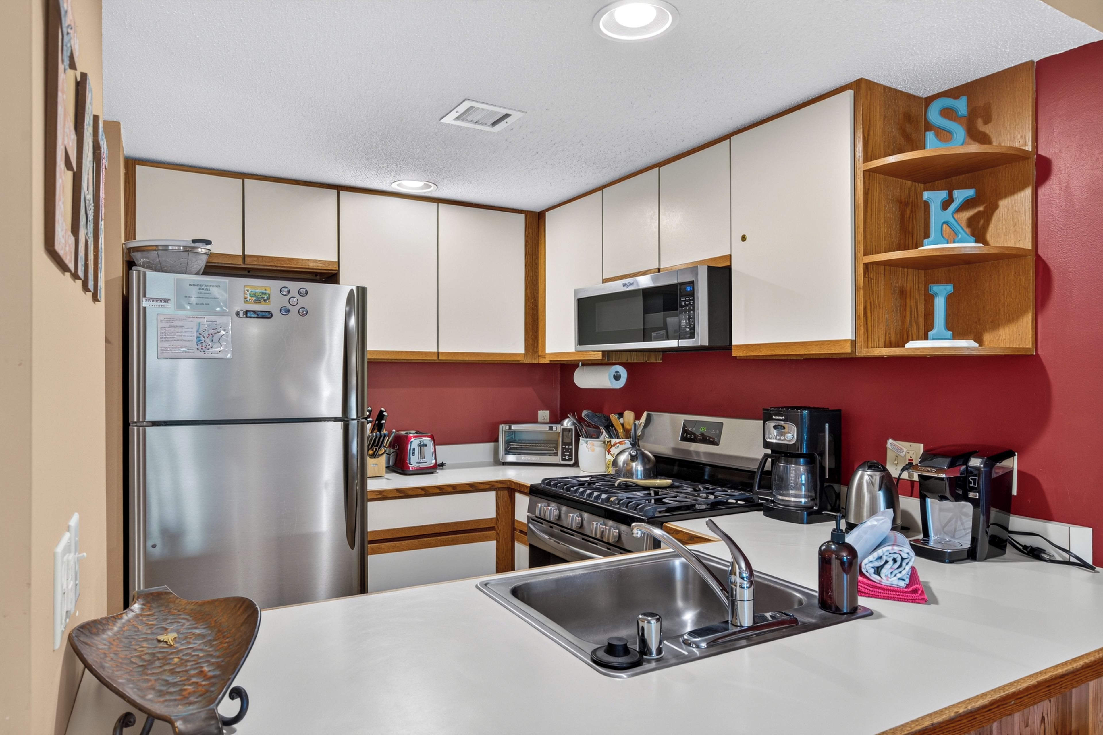 A modern kitchen with stainless steel appliances, wooden cabinets, and a red accent wall.