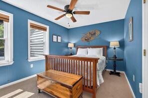 Un dormitorio con cama de madera, dos lámparas de noche, ventilador de techo y ventana con persianas.