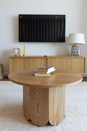 A round wooden table with books, a television mounted on the wall, a lamp, and a cabinet with a picture frame and a vase. - Wave 2.2 (Vila Nova de Gaia)