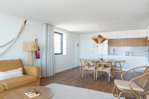 A modern living room with a sofa, coffee table, and dining area with chairs. There is a kitchen with white cabinets and a wooden countertop. - Wave 2.3 • Design and Conforto junto à Praia com AC (Vila Nova de Gaia)