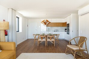 A modern kitchen with white cabinets, a dining table set for four, and a hanging light fixture. - Wave 2.3 • Design and Conforto junto à Praia com AC (Vila Nova de Gaia)