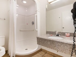 A bathroom with a shower, toilet, sink, and a hairdryer. - Knights Inn Tulsa (Tulsa)