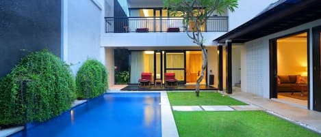 A modern two-story house with a swimming pool, a balcony, and a well-maintained lawn.