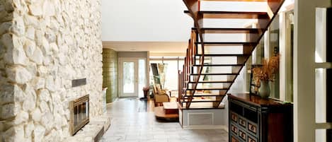 A spacious living area with a stone wall, a wooden staircase, and a fireplace.
