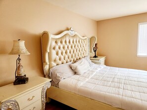 A bedroom with a tufted headboard, a bedside table with a lamp, and a nightstand with a mirror.