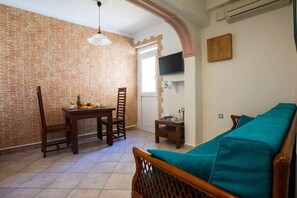 Una habitación con pared de ladrillo, una mesa de comedor con sillas, un sofá color turquesa y un televisor montado en la pared.