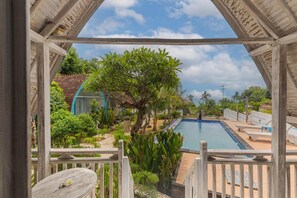 Uma área de piscina com deck de madeira, espreguiçadeiras e vista para um jardim com árvores e um edifício ao fundo.