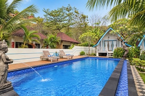 A swimming pool with lounge chairs, a statue, and a building with a blue roof.