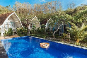 Piscina com uma cesta flutuante, cercada por vegetação exuberante e edifícios de estilo tradicional.