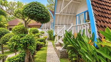 A pathway leading to a building with a covered porch, surrounded by lush greenery and a small tree.