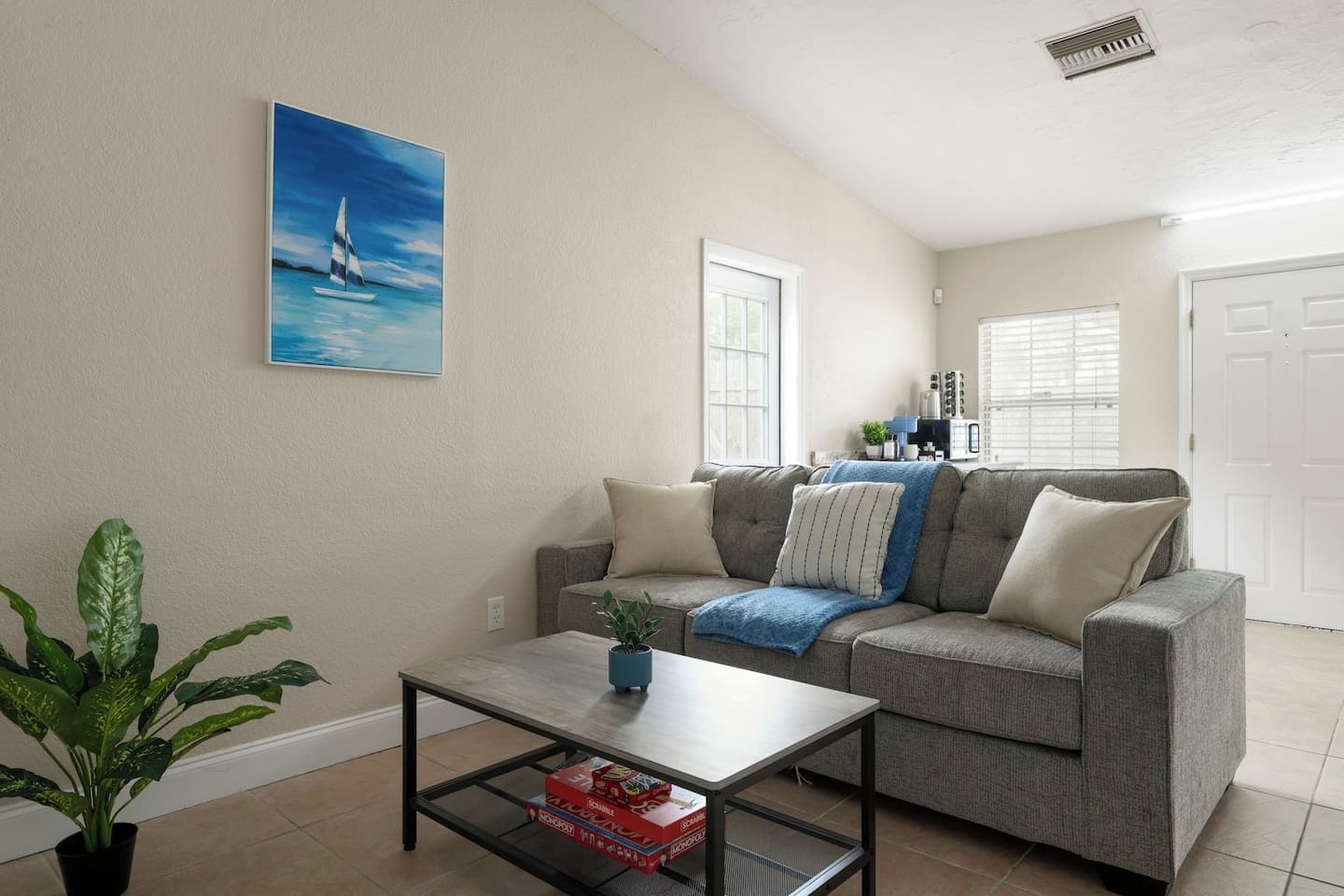 A living room with a gray sofa, a coffee table, a potted plant, and a painting on the wall.