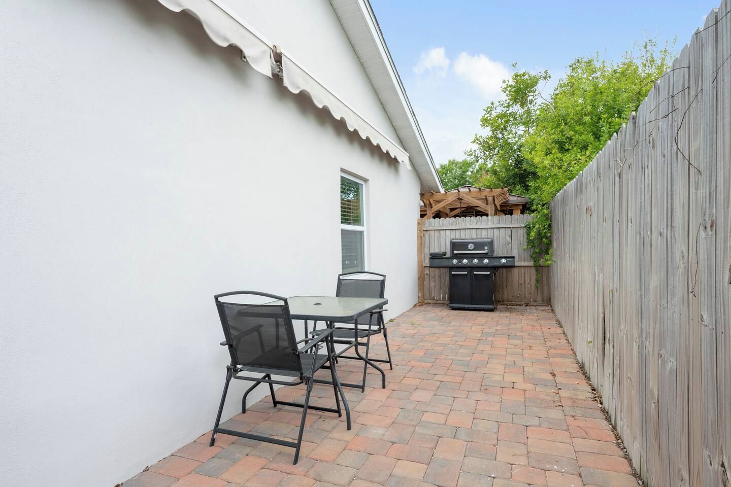A patio with a table and chairs, a grill, and a wooden fence.