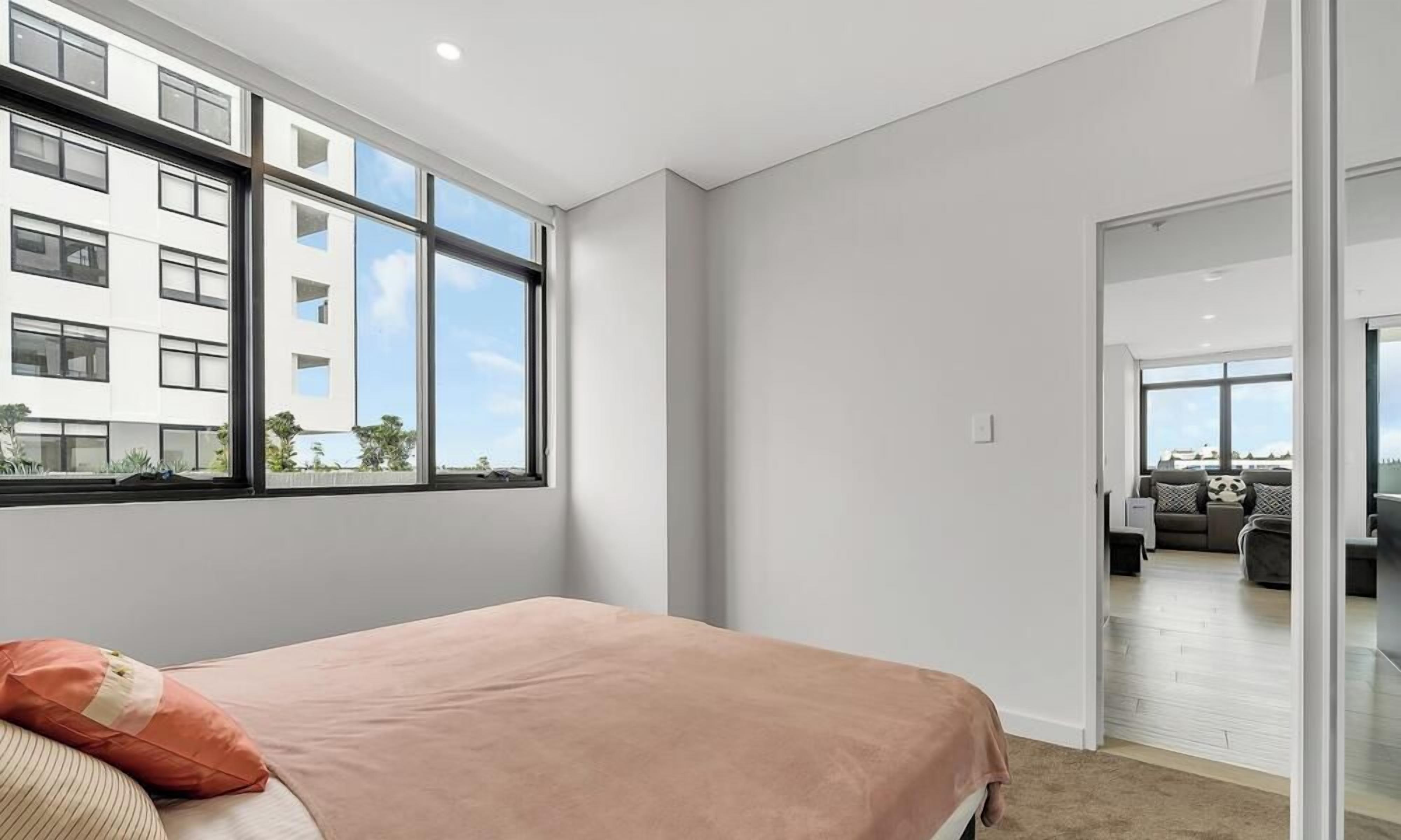A modern bedroom with a large window, a bed with a pink blanket, and a view of a cityscape.