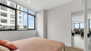 A modern bedroom with a large window, a bed with a pink blanket, and a view of a cityscape.