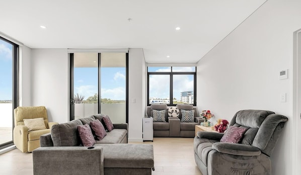 A modern living room with a sofa, armchairs, and a coffee table. There are large windows providing a view of the city. - KozyGuru | Fairfield | Stylish Stay Near Station (Fairfield)