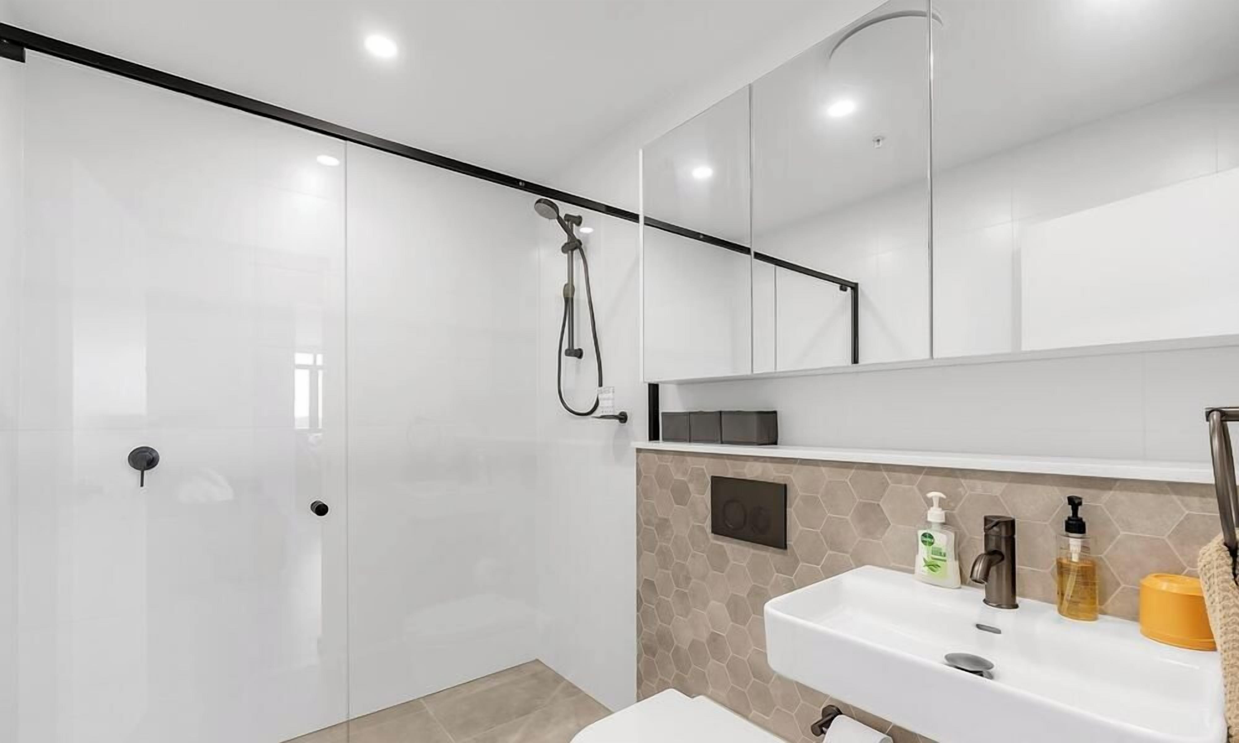A modern bathroom with a glass shower enclosure, a white sink with toiletries, and a large mirror above the sink.
