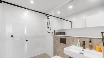 A modern bathroom with a glass shower enclosure, a white sink with toiletries, and a large mirror above the sink.