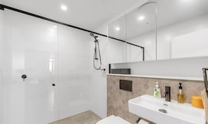 A modern bathroom with a glass shower enclosure, a white sink with toiletries, and a large mirror above the sink. - KozyGuru | Fairfield | Stylish Stay Near Station (Fairfield)