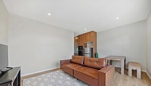 A modern living room with a leather sofa, a flat-screen TV, a dining table, and a kitchen area in the background. - KozyGuru | Cobbitty | Serene Granny Flat Escape (Cobbitty)
