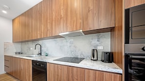 A modern kitchen with wooden cabinets, a stainless steel kettle, a toaster, and a dishwasher. - KozyGuru | Cobbitty | Serene Granny Flat Escape (Cobbitty)