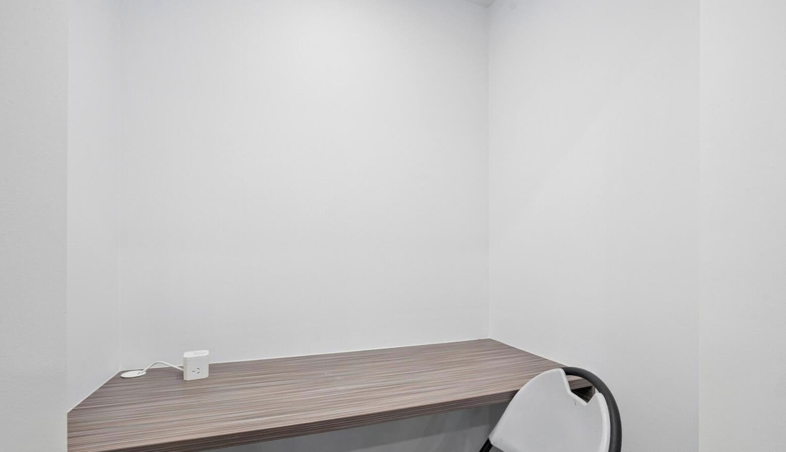 A minimalist office space with a wooden desk, a chair, and a white wall.